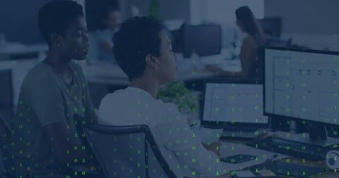 Female Colleague Collaborating at Dual-Monitor Desk with Binary Data Overlay in Open Office