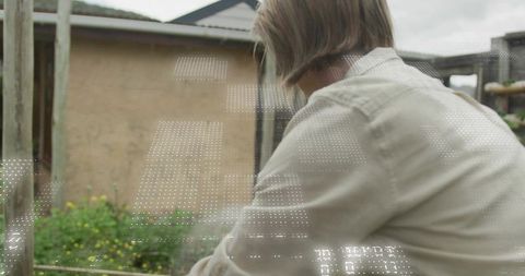 Mature woman tending small backyard garden by trellis and wooden posts, outdoor lifestyle