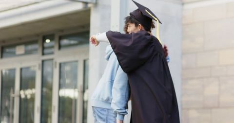 Diverse friends hugging graduate on campus celebrating achievement in gown and mortarboard