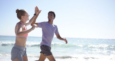Energetic Pair Giving High-Five While Jogging on Sunny Beach
