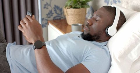 Man Relaxing on Bed with Headphones and Smartphone