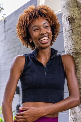 Joyful african woman laughing while leaning on tree in sunlit courtyard