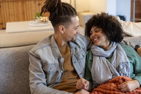 Young couple sharing cozy moment on sofa with warm throw, soft ambient lighting, smiling