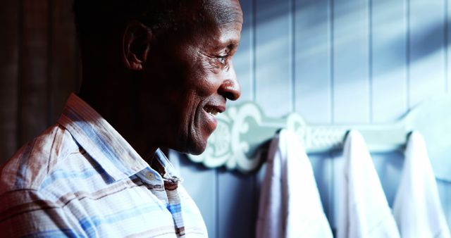 Elderly man smiling warmly indoors, creating a cozy and uplifting scene. Ideal for use in projects related to senior well-being, happiness in old age, and family moments. This image can be used in advertisements, blogs, or articles focusing on positive lifestyles for older adults.