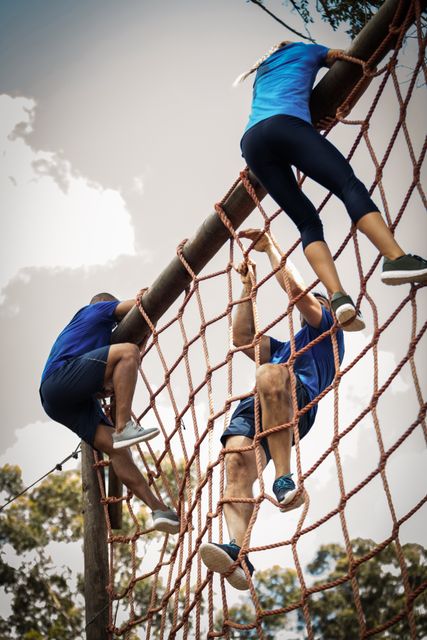 Participants climbing a net during an outdoor obstacle course in a boot camp. Ideal for illustrating teamwork, physical fitness, and outdoor adventure activities. Useful for fitness programs, team-building events, and sports training promotions.