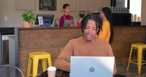 African american man working on laptop in cozy modern cafe with barista and patrons