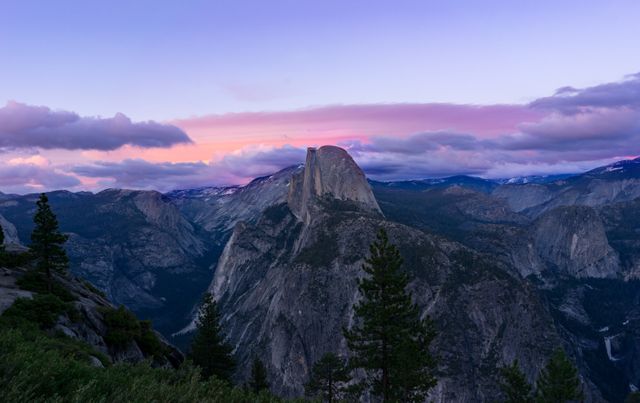 Majestic view of Half Dome during sunset in Yosemite National Park. The sky features vibrant colors contrasting with the silhouette of the mountain. Ideal for backgrounds, travel promotions, nature documentaries, and inspirational content.
