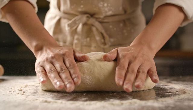 Home baker shaping artisan bread dough on floured countertop kneading hands warm light