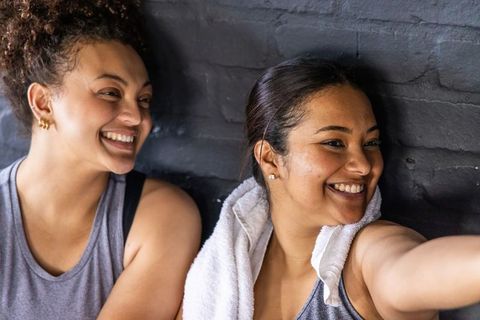 Two women smiling and reaching for camera after workout, gym camaraderie and fitness