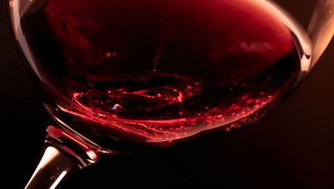 Swirling deep ruby wine in crystal glass close-up macro with glowing rim highlights