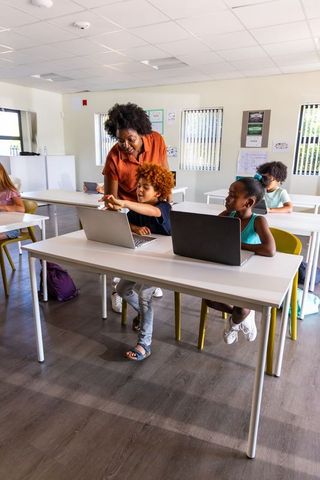 African american teacher guiding red-haired student using laptops in bright modern classroom