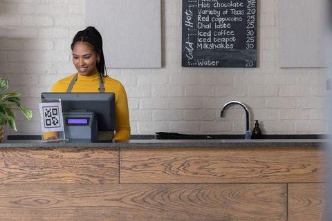 African american barista operating touchscreen pos at minimalist cafe counter smiling