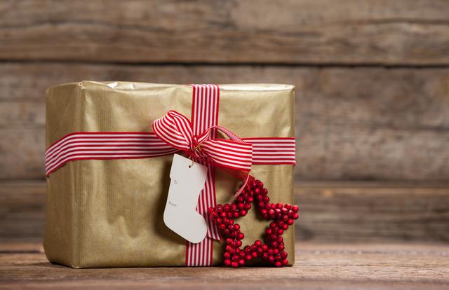 Gift box wrapped in gold paper with red and white striped ribbon and star ornament on wooden table. Ideal for holiday promotions, Christmas advertisements, festive greeting cards, and seasonal blog posts.