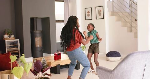 African mother and daughter dancing joyfully in modern living room with retro red radio