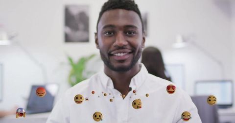 Smiling Businessman Surrounded by Floating Emojis in Modern Office