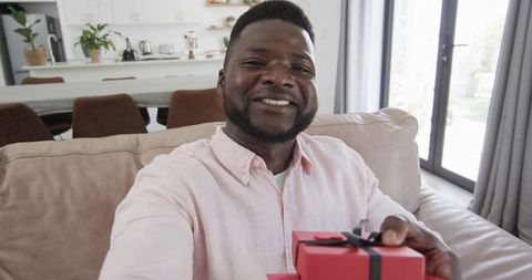Smiling man holding gift box in cozy living room