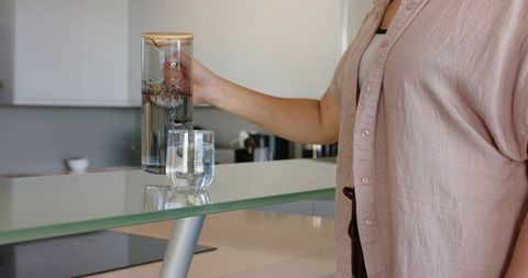 Reaching woman placing herbal infusion carafe on glass kitchen island with copy space