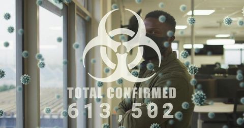 Standing masked black man crossing arms in modern office with biohazard overlay
