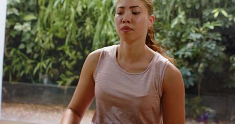 Young woman exercising in home studio with glass wall and lush indoor greenery