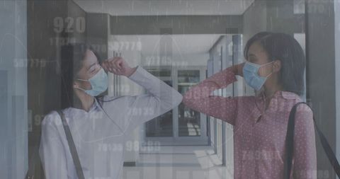 Two business colleagues wearing masks are greeting each other with an elbow bump indoors, reflecting pandemic-era changes in workplace etiquette. This is suitable for content focusing on health protocol adherence, pandemic impacts on business interactions, or modern workplace communication.