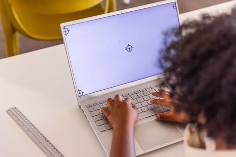 African american girl typing on laptop at classroom desk with ruler, remote learning focus