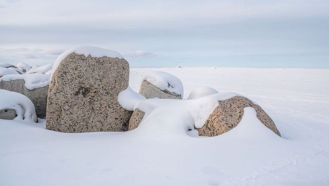 Granite boulders draped in snow on frozen tundra with low horizon and soft sky minimalist