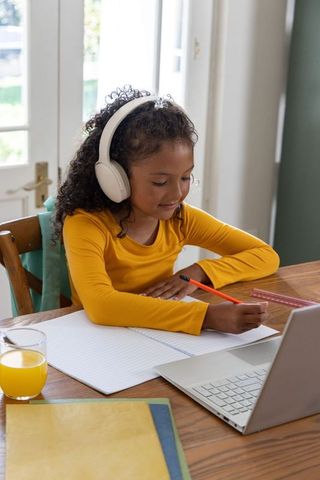 African american girl studying at table with headphones, laptop, notebook, orange juice