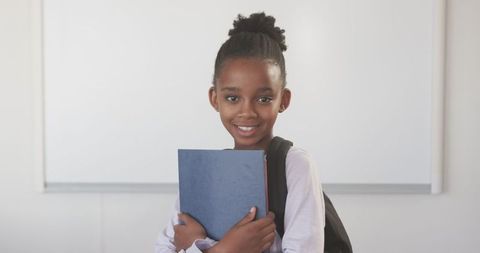 Smiling african american girl holding notebook in classroom environment