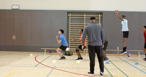 Youth volleyball team practicing explosive jumps and agility drills with coach in indoor gym