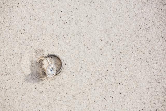 Close-up image of a pair of wedding rings on sandy beach. Ideal for use in wedding invitations, beach-themed wedding promotions, jewelry advertisements, or engagement announcements.