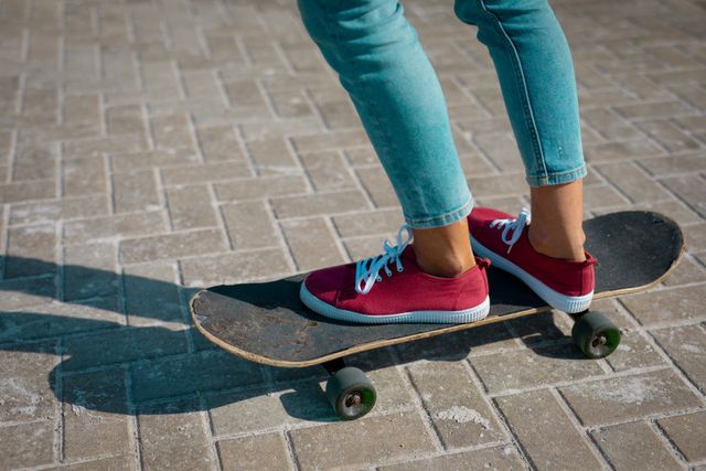 Low section of biracial woman wearing trainers standing on skateboard. outdoor healthy active lifestyle.