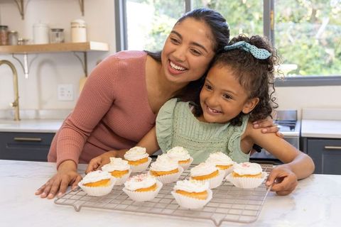 Mother and daughter baking and decorating cupcakes on sunlit marble kitchen island
