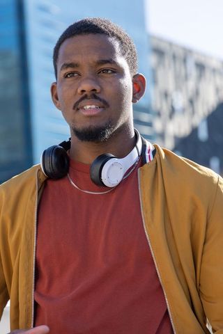 African american man standing in urban plaza wearing headphones and mustard zip jacket