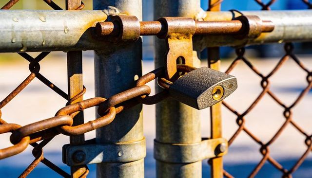 Rectangular padlock securing rusted chain on metal gate close-up showing weathered texture