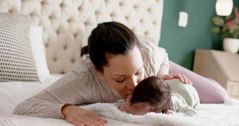 Mother Lovingly Kissing Newborn on Bed at Home