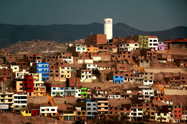 Bright colorful houses of varying sizes on a hillside in a vibrant urban community with mountains in the background captured during daytime. Ideal for articles on urban diversity, architecture, South American cultures, or residential areas. Useful for design projects needing injection of vivid colors and cultural richness.