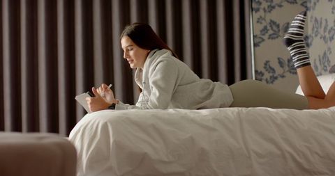 Young Woman Relaxing on Bed Writing in Notebook at Home