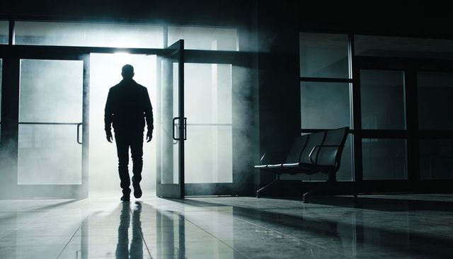 Backlit male silhouette walking through glass doors into foggy lobby with reflective floor