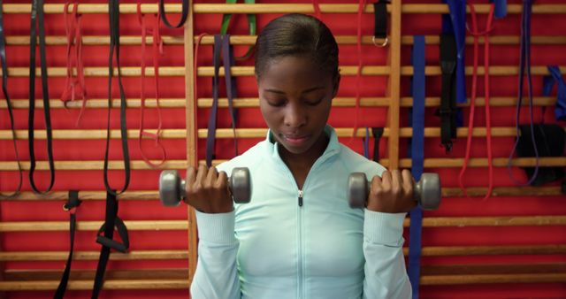 Young African American woman lifts weights at the gym. Her focus on fitness highlights a commitment to health and well-being.