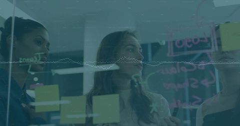 Team brainstorming and writing on glass board with sticky notes, collaborating in office