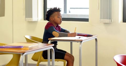 Young Boy Focused Studying at Classroom Desk Near Window