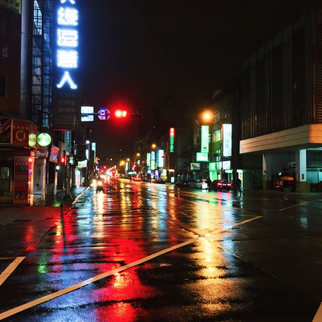 Wet street glowing with neon lights reflecting on rainy night in city. Ideal for content on urban nightlife, rainy weather, cityscape, and vibrant, atmospheric shots.
