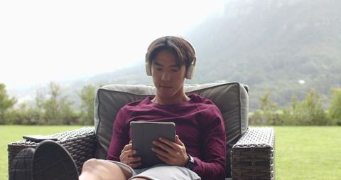 Man Relaxing Outdoors Using Tablet with Headphones in Scenic Garden