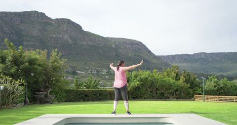Mature woman stretching on pool edge with mountain view for outdoor fitness and wellness