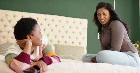 Diverse friends chatting casually on bed with smartphone