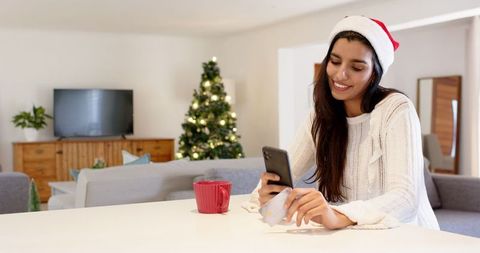 Festive Indian Woman Using Phone Near Christmas Tree at Home