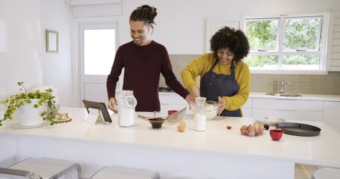 Couple baking together in bright modern kitchen sharing recipe and mixing batter