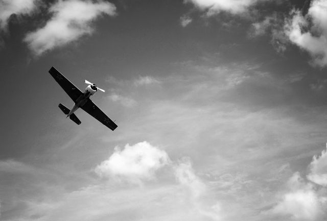 Vintage airplane soaring through a partly cloudy sky captured in black and white. Ideal for use in historical, aviation, travel, and nostalgia-themed projects. Perfect for backgrounds, prints, and educational materials emphasizing retro aviation.