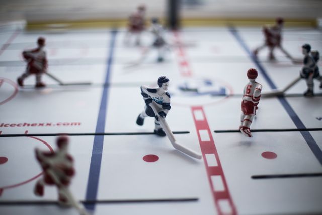 Close-up view of miniature hockey players on a table hockey game board engaging in a dynamic play moment. Great for themes related to games, indoor activities, childhood, sports fandom, or miniature collections.
