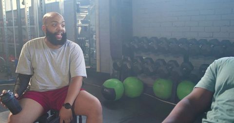 African american men resting on gym bench chatting while holding shaker bottle and workout gear